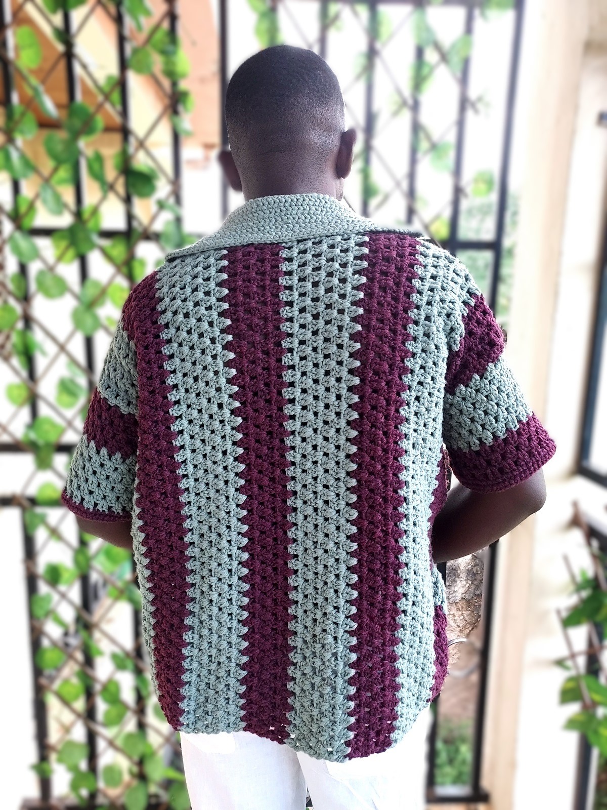 Vue arrière d'un homme portant une chemise en crochet fait main à rayures verticales texturées à boutons.